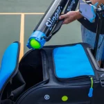 Tennis player using Slinger Bag Ball Collector Tube to collect tennis balls on court without bending over